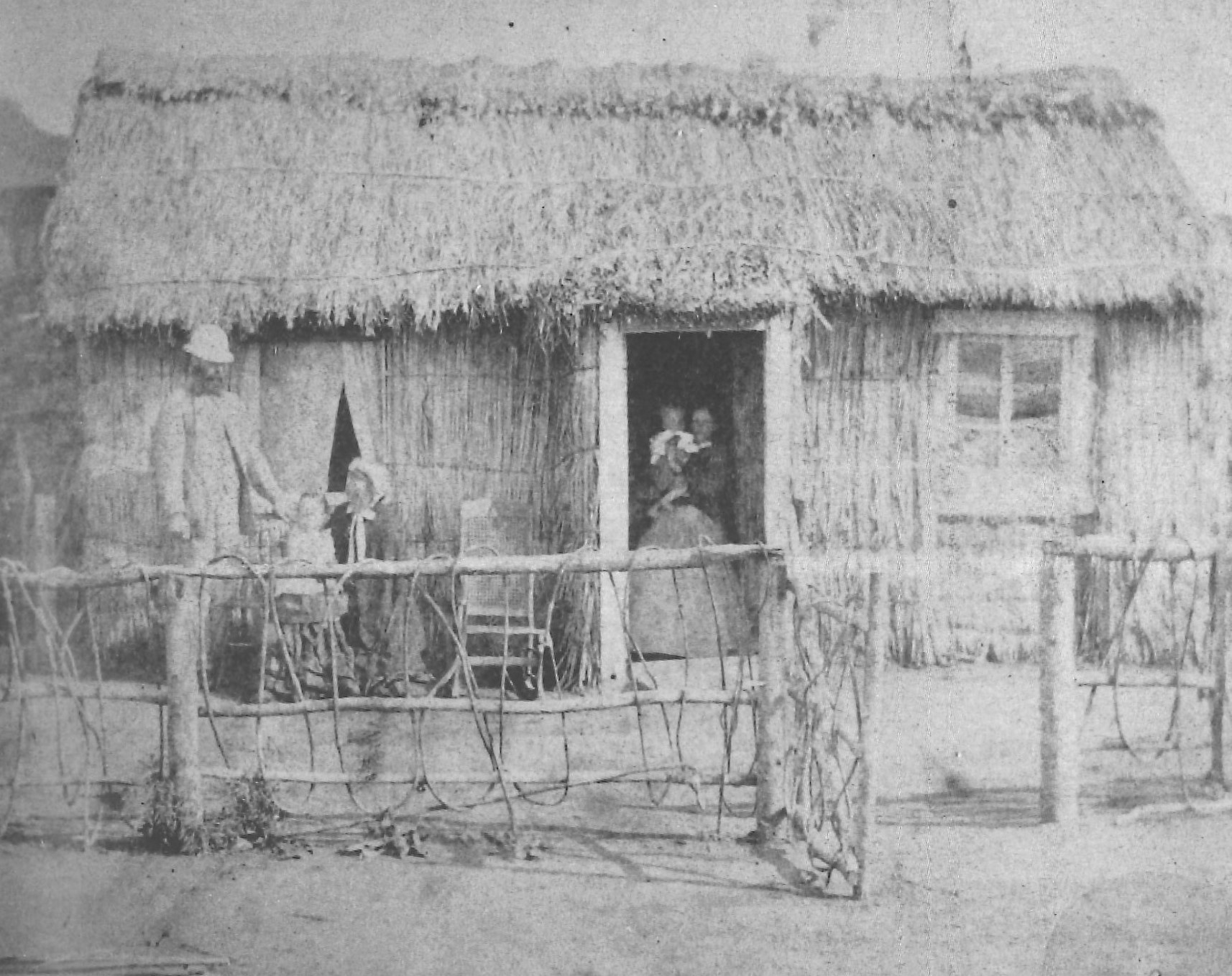 The Gascoyne whare at Pukearuhe Redoubt with Bamber Gascoyne, Mrs de Webber and toddler Laura on the left and Annie Gascoyne holding baby Cecil in the doorway (1868). Image from the book "Strangerland: a family at war" by Helena Drysdale.